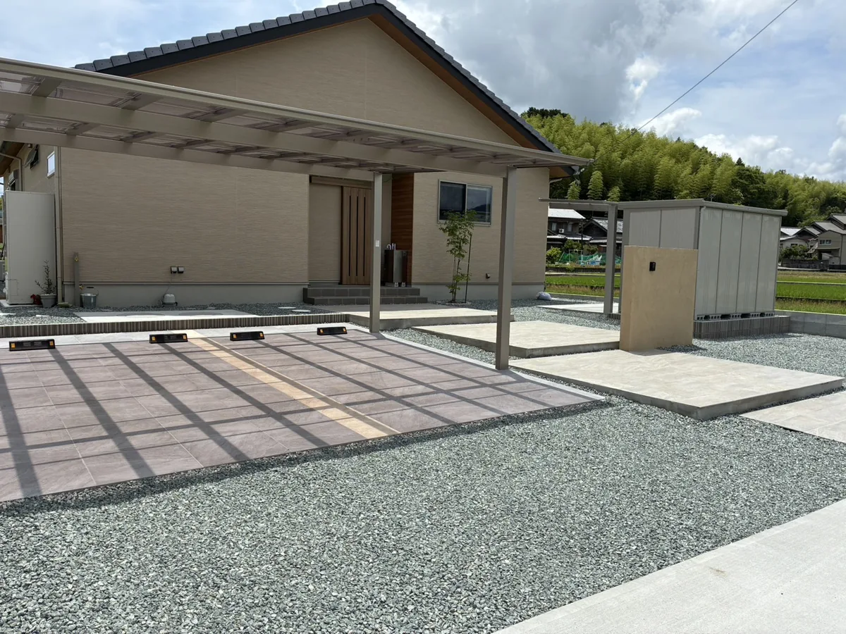 平屋住宅の新築外構。2台用カーポートとタイル貼りの駐車スペース、塗り壁の門柱、砂利敷き